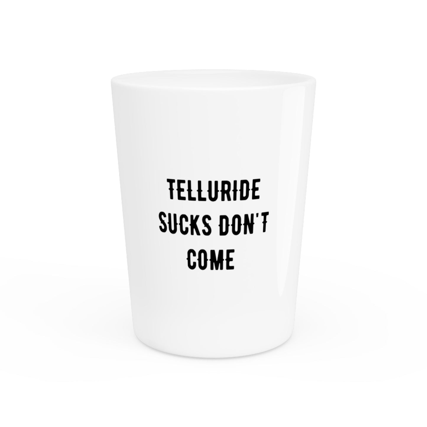 White ceramic shot glass with black lettering saying "Telluride Sucks Don’t Come.” The shot glass is perfect for enjoying a shot of your favorite spirit at the Telluride Ski Resort or anywhere else you enjoy spending time in the great outdoors. The phrase "Telluride Sucks Don’t Come” is a humorous way to express your love of skiing and snowboarding, and the amazing town that you want to keep to yourself.