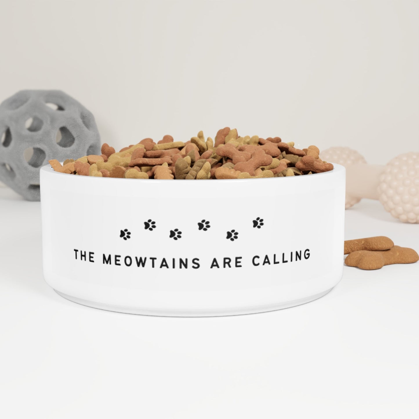 White ceramic cat bowl with black lettering saying "The Meowtains are Calling." The bowl is perfect for feeding your cat while they dream of exploring the great outdoors. The text is a humorous play on words that is sure to make cat lovers laugh. This is a great way to show your love for the mountains and for the Telluride Ski Resort. 